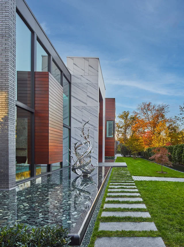 Urban Woodland House exterior with a mixed material facade and reflecting pond, surrounded by autumn landscaping.