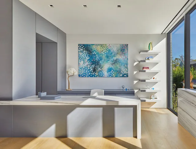 Office room with built-in shelving and a large floor-to-ceiling window showing garden outside.