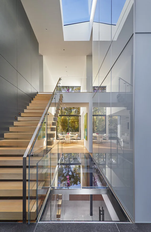 Modern interior features a floating wooden staircase with glass railings and a large skylight overhead.