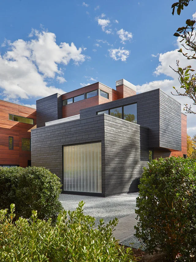 The URBAN WOODLAND HOUSE features a mixed-material facade with dark brick and wood siding reflecting a contemporary design.