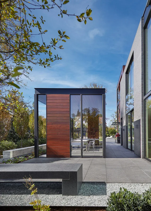 Outdoor patio features a wood-paneled glass structure next to a multi-story modern building with large windows.