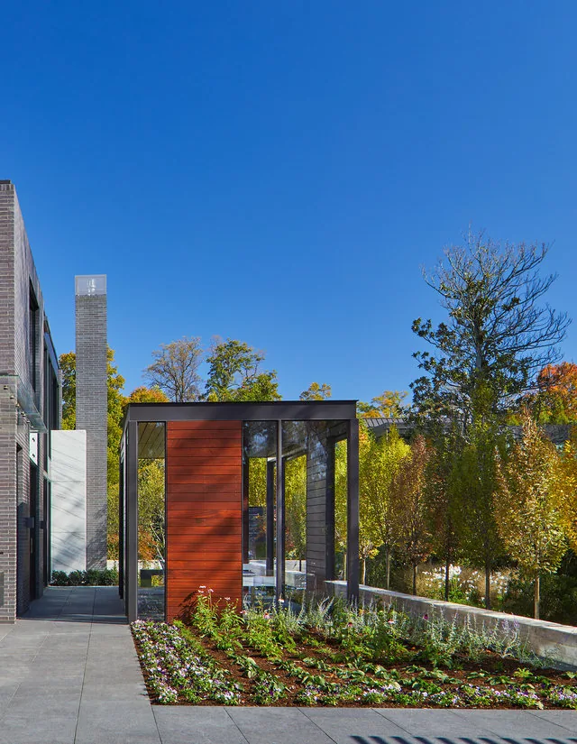 The URBAN WOODLAND HOUSE features a glass and wood pavilion alongside a garden bed, designed by Robert Gurney Architects.