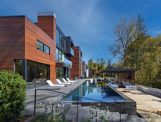 The URBAN WOODLAND HOUSE features wood siding and an outdoor pool area with lounge seating and a covered patio space.
