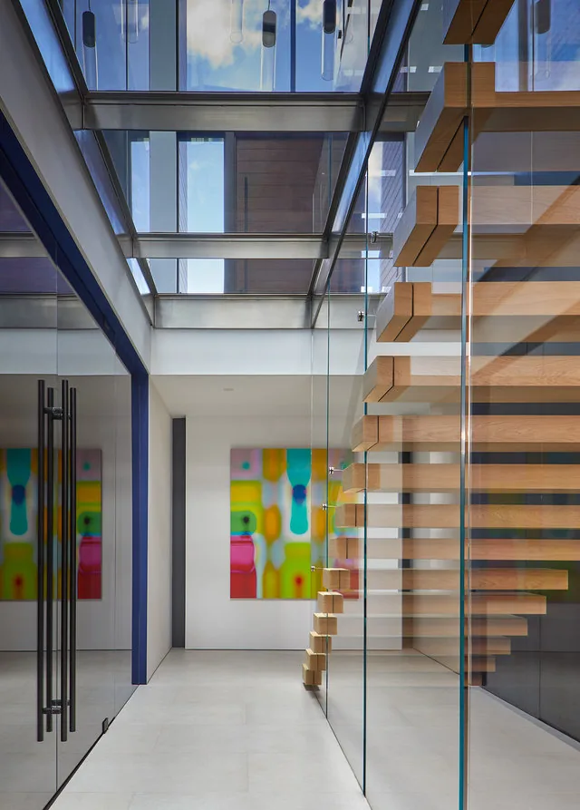 Floating wood staircase enclosed in glass, positioned under a large glass ceiling allowing natural light in.