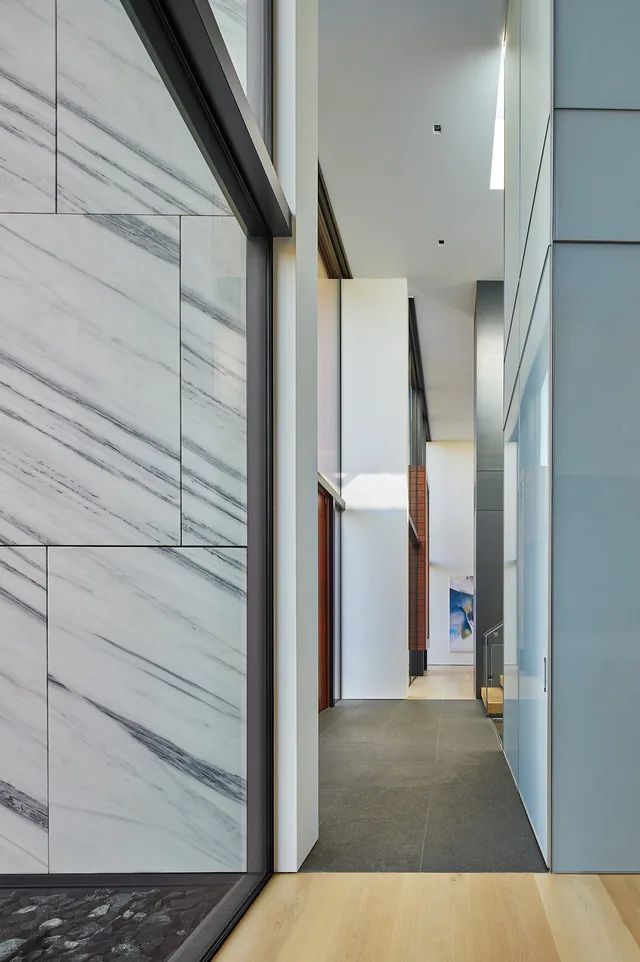 Interior hallway features a large marble wall detail and contrasting flooring materials in the Urban Woodland House.