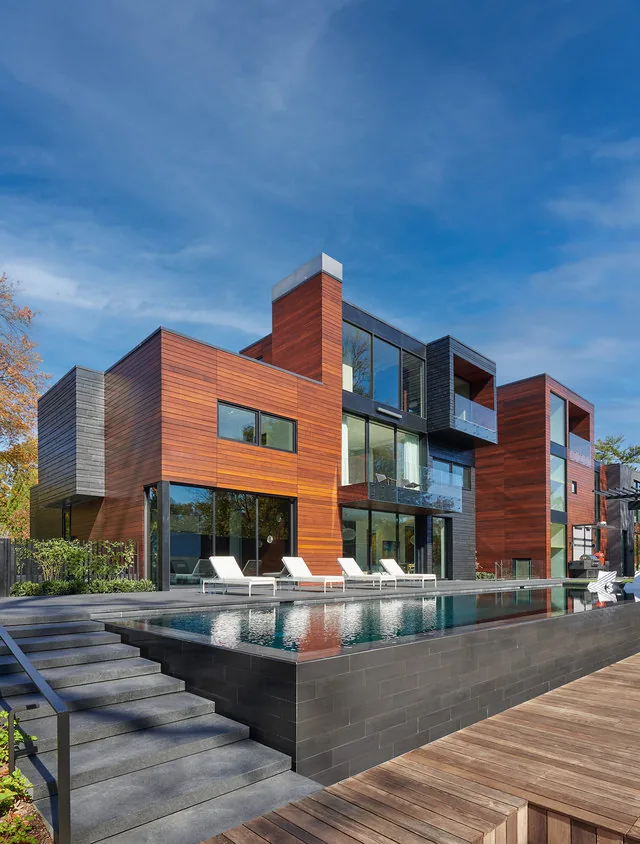 URBAN WOODLAND HOUSE features wood siding, glass railings, and a rectangular pool with outdoor lounge chairs by Robert Gurney Architects.