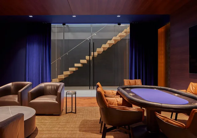 Game room features a poker table, leather seating, and a floating stair visible through glass doors.