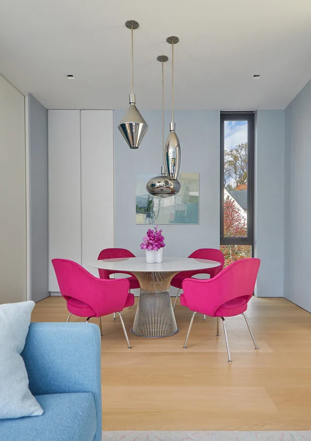 Dining area with vibrant pink chairs and a round table accented by three unique metallic pendant fixtures.