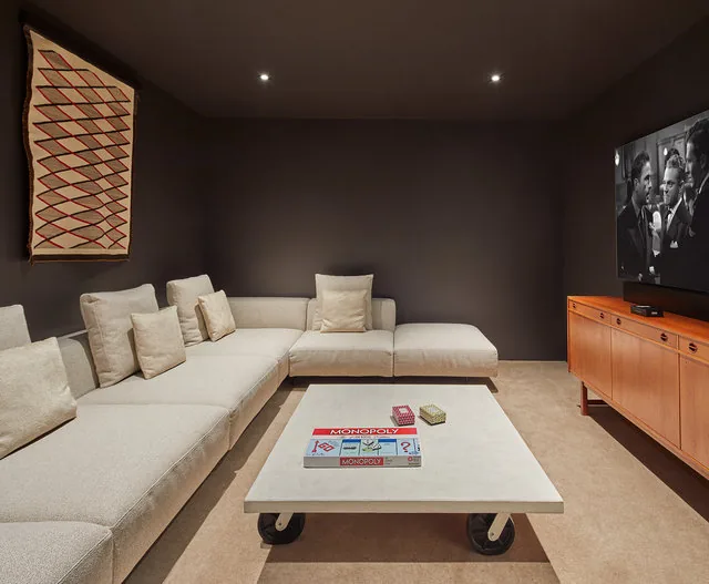 Living room features a beige sectional sofa, rolling coffee table, and a wooden credenza supporting a TV playing a classic black and white film.
