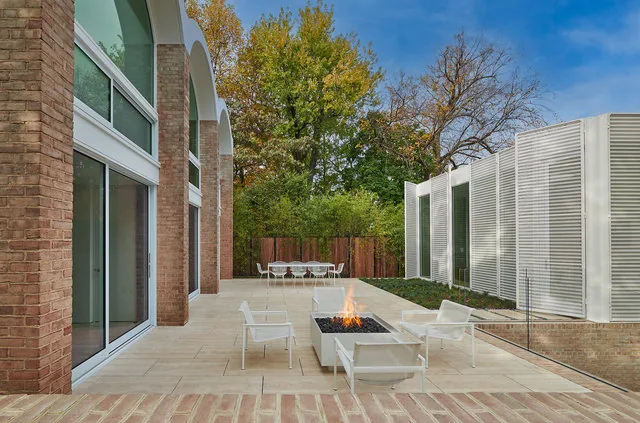 Patio features a fire pit with white modern outdoor chairs, brick privacy wall with arched openings, and white privacy panels.