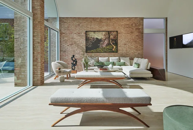 Living room features vaulted ceiling, exposed brick wall, and glass curtain walls providing outdoor view.