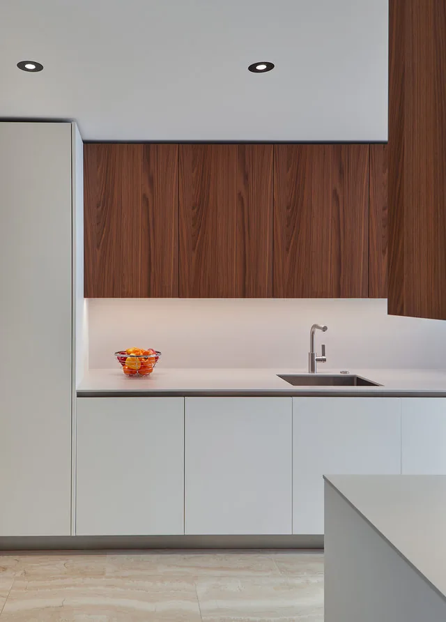 Kitchen view showing wood upper cabinets and white lower cabinets with a countertop and sink.