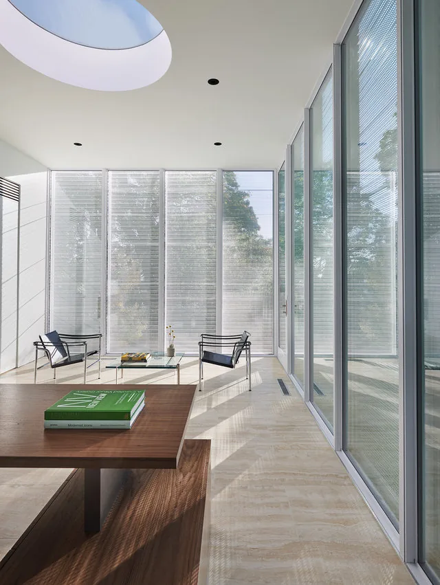 Modern room featuring large floor-to-ceiling glazing, a circular skylight, and minimalist furniture.