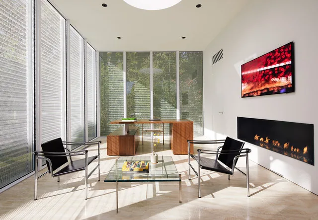 Modern sitting area features black leather chairs, a glass coffee table, and a wall-mounted linear fireplace with floor-to-ceiling windows.