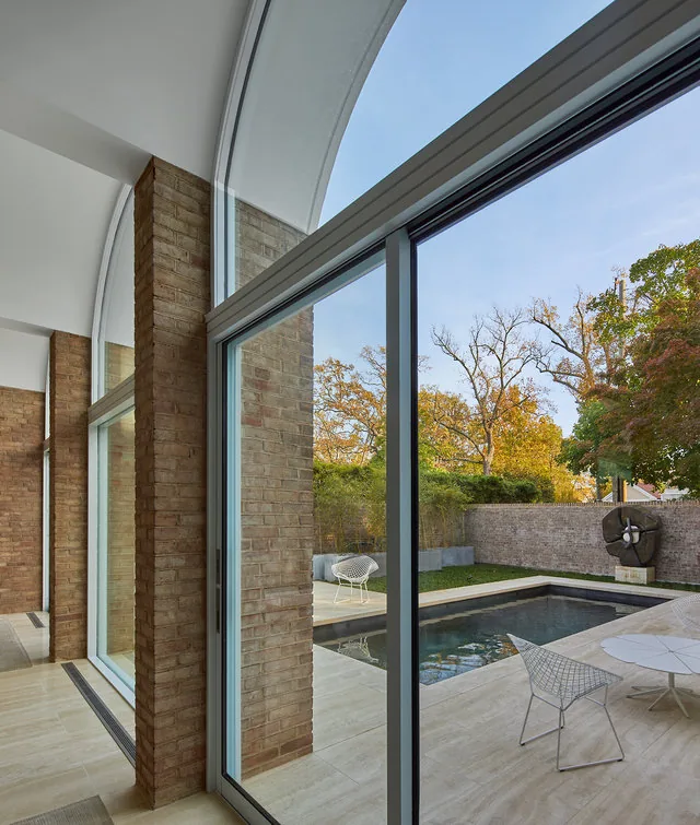 The Slayton House renovation features large arched windows and sliding glass doors opening to a serene pool courtyard.