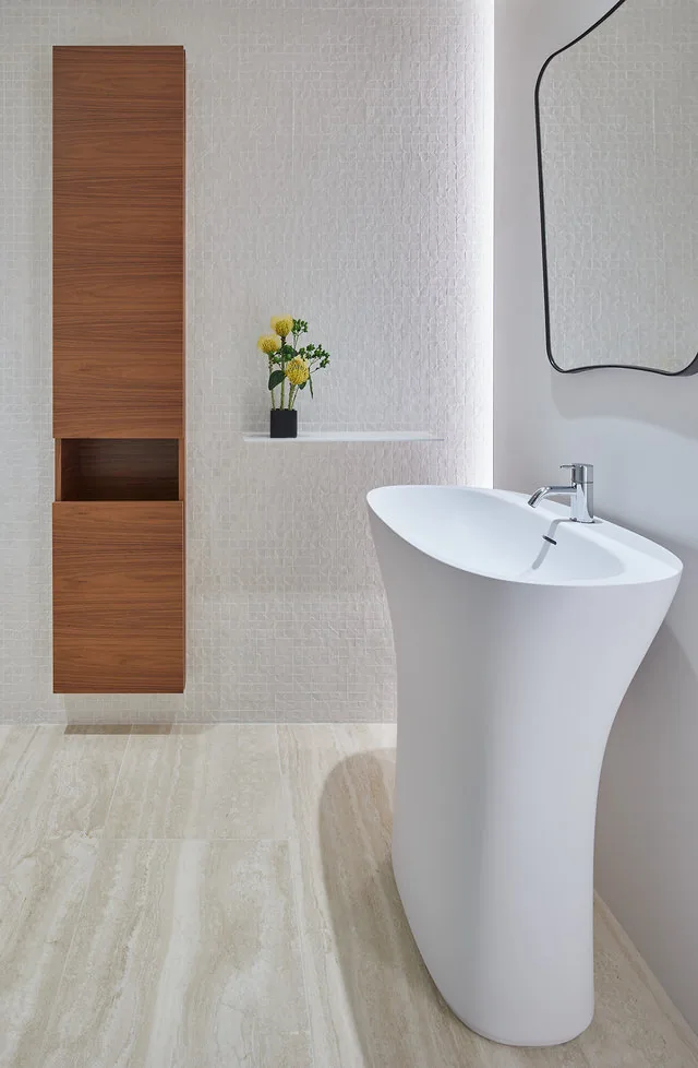 Pedestal sink in a modern bathroom alongside a tall wood cabinet and a textured accent wall.