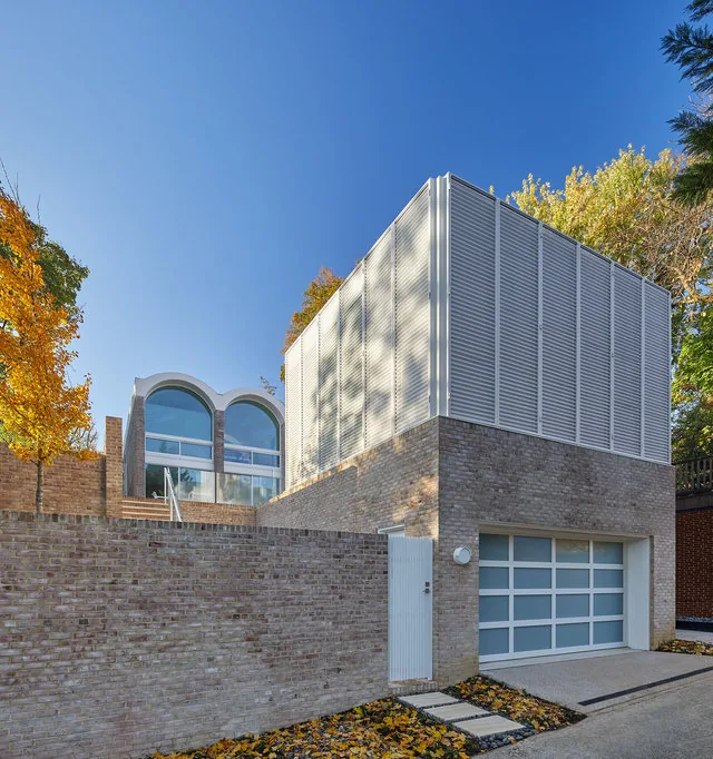 SLAYTON HOUSE RENOVATION AND ADDITION features arched windows and a brick exterior with a garage and frosted glass door.