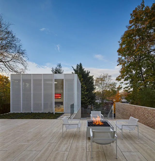 Patio with fire pit and white outdoor seating next to a modern structure with vertical slat cladding and glass curtain walls.