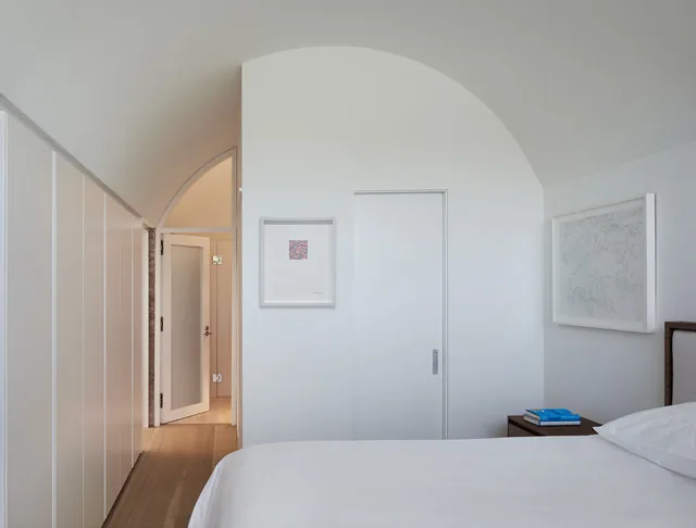 Bedroom with curved white ceiling, recessed lighting, and framed art on white walls.
