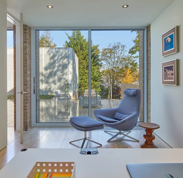 A blue lounge chair with ottoman sits in front of sliding glass doors leading to a tiled outdoor patio with metal chairs.