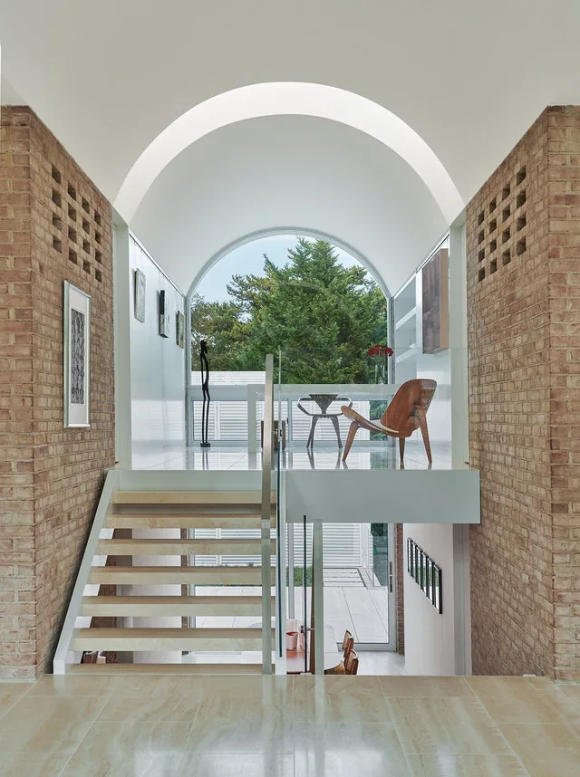 The Slayton House renovation features a white barrel vault ceiling between exposed brick walls with an open stair connecting levels.