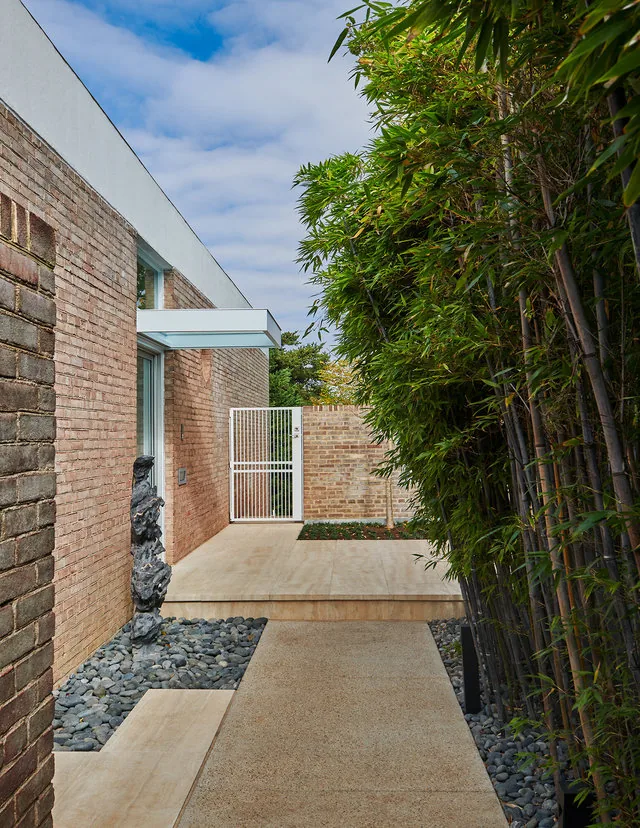 Exterior corridor of the Slayton House renovation with brick walls, bamboo, and a white metal gate.