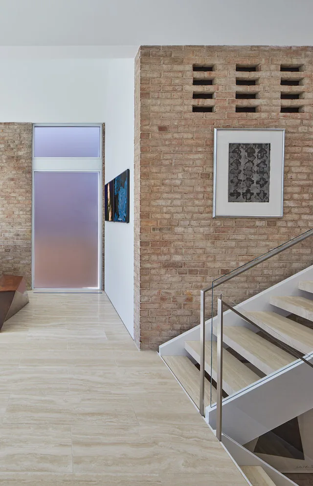 View of a staircase with glass railing next to an exposed brick wall and framed artwork in the SLAYTON HOUSE RENOVATION AND ADDITION.