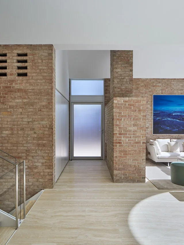 Exposed brick interior hallway features light wood floors and natural light through frosted glass and clerestory windows.
