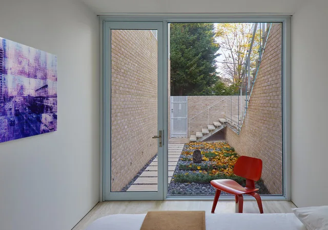 Sunken garden and outdoor staircase visible through floor-to-ceiling glass door in a bedroom.