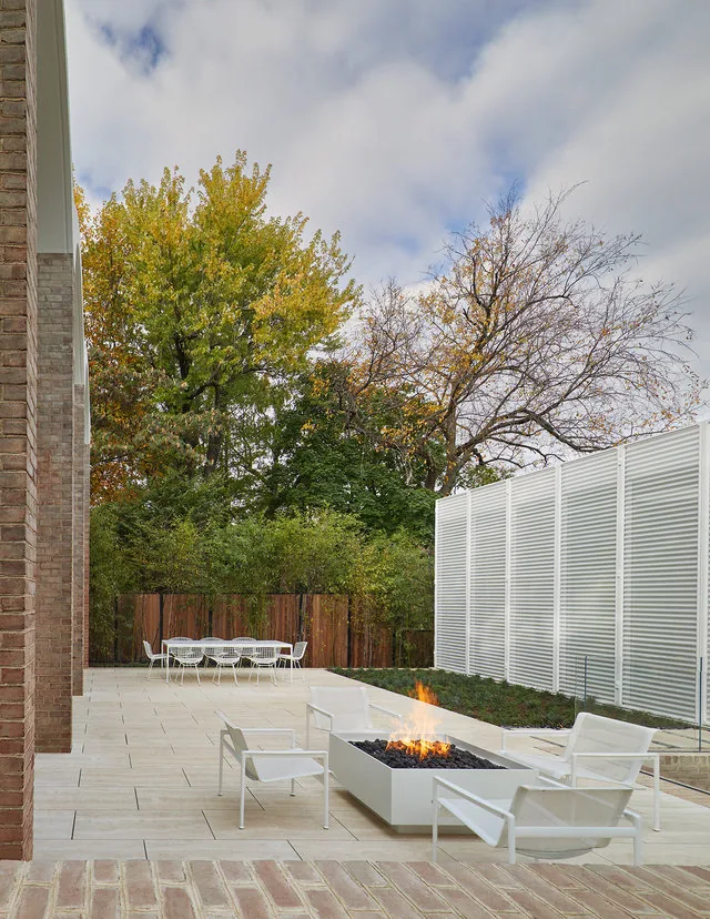 The outdoor patio features a rectangular fire pit with seating and a dining area adjacent to a wooden privacy fence.