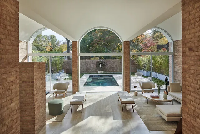 The renovated living area features white vaulted arches and large arched openings looking out to a reflecting pool and brick privacy wall.