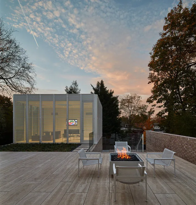 The Slayton House features a modern white metal chair seating area around a rectangular fire pit on a large tiled patio.