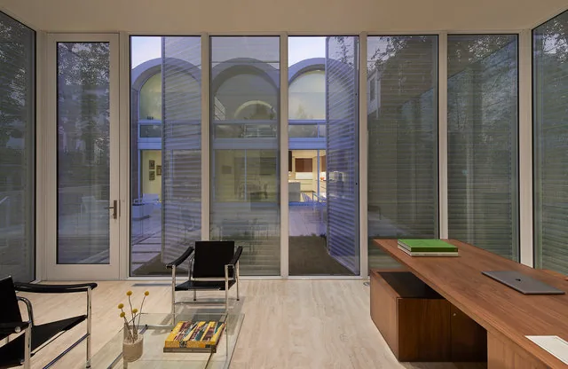 Modern office with floor-to-ceiling glazing overlooking courtyard with vaulted arches and a fire pit in the background.