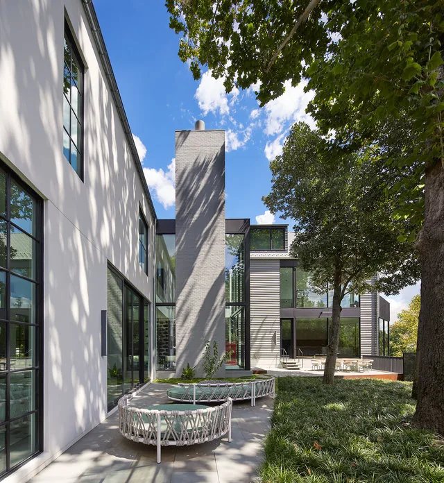 The Phillips Park House features a spacious exterior patio with modern round seating and floor-to-ceiling glazing.