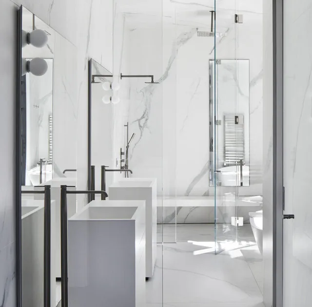 The Phillips Park House bathroom by Robert Gurney Architects features marble walls, dual sinks, and a glass shower enclosure.