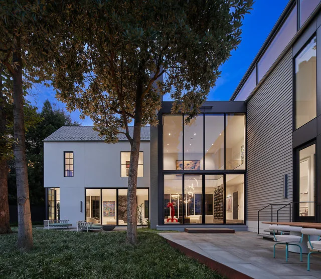 PHILLIPS PARK HOUSE features large grid windows and a white exterior wall with a spacious patio area at dusk.