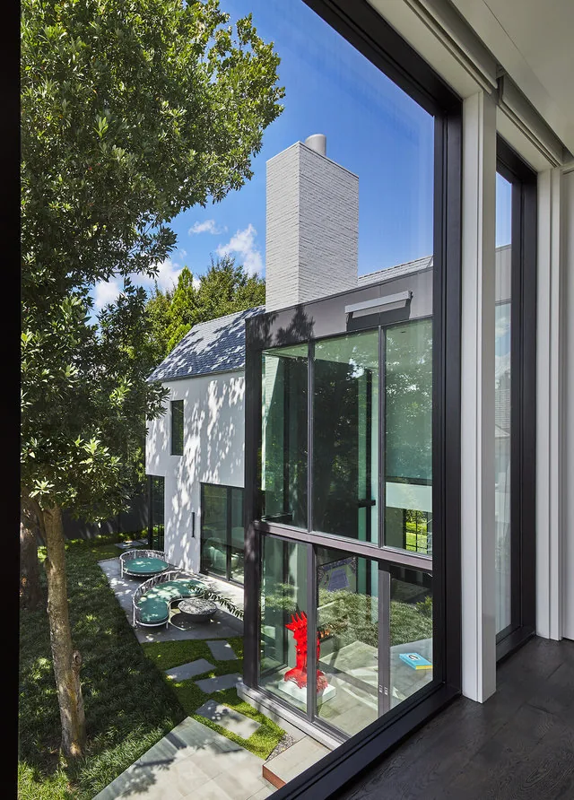Exterior view of the Phillips Park House showing a white chimney, large floor-to-ceiling windows and a patio with curved seating.