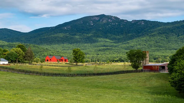 ETLAN FARM HOUSE features red exterior siding and black wooden fencing in a rural pasture setting with mountain views.