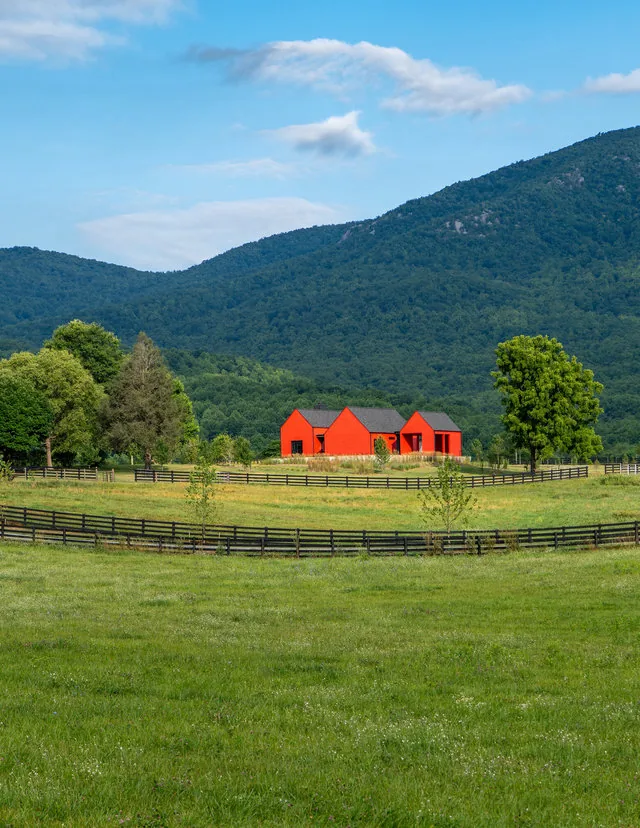 ETLAN FARM HOUSE by Robert Gurney Architects features a red exterior with three steep gable roofs in a pastoral rural setting.