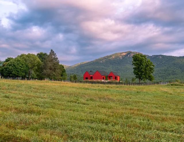 The ETLAN FARM HOUSE by Robert Gurney Architects features red exterior siding and a black wooden fence, set in a rural pasture with a mountain view.