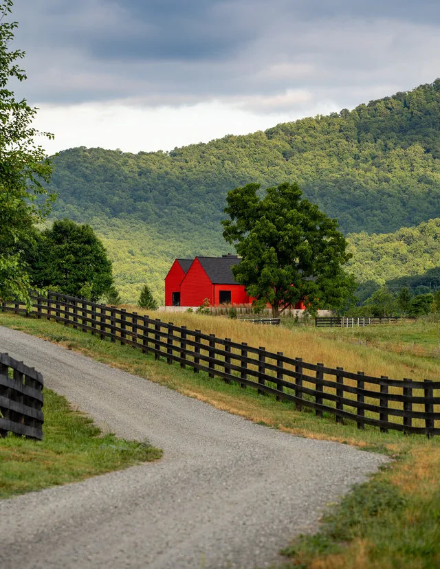 ETLAN FARM HOUSE features a red exterior siding with a black gable roof, set in rural pasture with mountainous green backdrop.