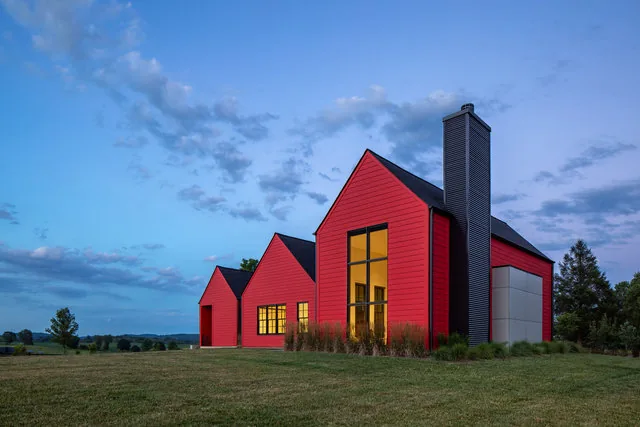 ETLAN FARM HOUSE features three red gabled volumes with large windows and a chimney in a rural setting.