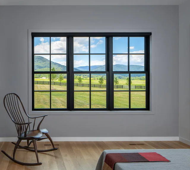 Black-framed window with divided lites frames a rural pasture and mountain view from the bedroom of ETLAN FARM HOUSE.