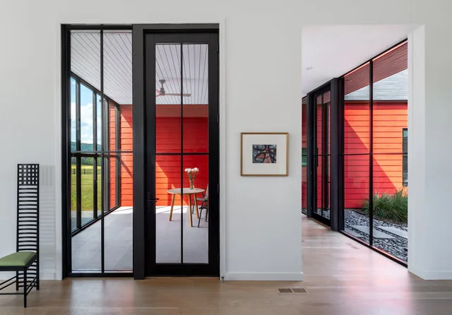 Black-framed glass doors open to a covered patio with red siding in this farmhouse entry area.