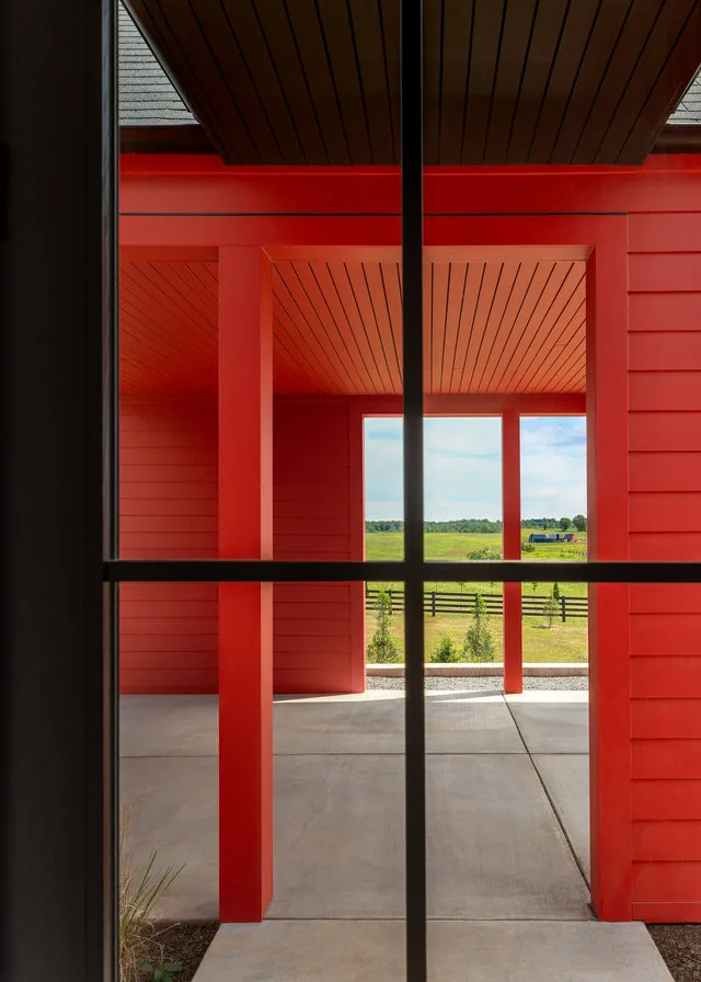 The ETLAN FARM HOUSE features a red exterior porch with wood slatted ceiling and posts framing a countryside pasture view.