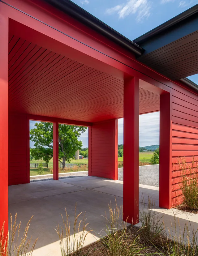 The ETLAN FARM HOUSE features a bold red exterior carport opening to fenced pasture and mountain views.