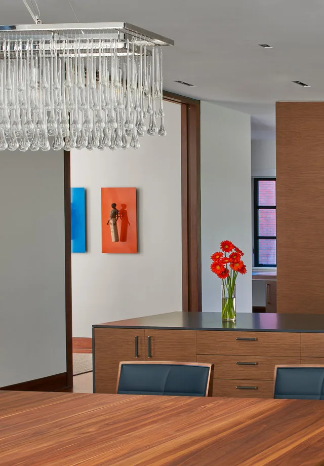 Dining area featuring a large wood table, black chairs, and a contemporary glass chandelier, with colorful artwork on the wall beyond.