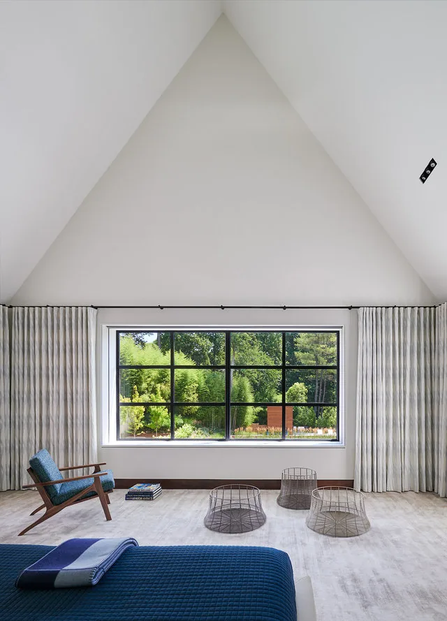 Bedroom with vaulted ceiling, large grid window with black frames, and light-colored carpet floor.