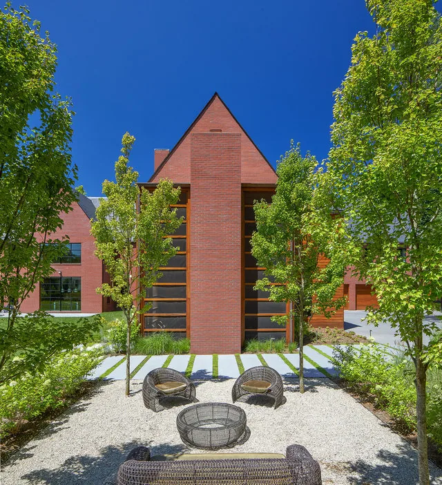The outdoor seating area features modern wicker furniture in front of a red brick home with a steep gable roof and large vertically divided windows.
