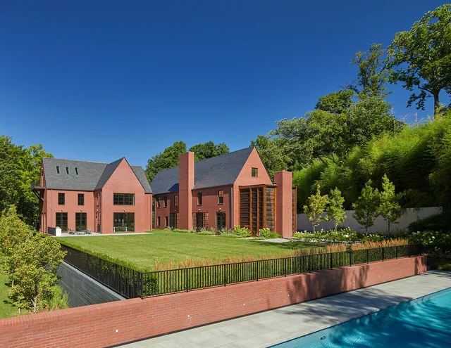 30TH STREET HOUSE features steep roof pitches and brick exterior with large vertical window panels facing a pool and lawn.